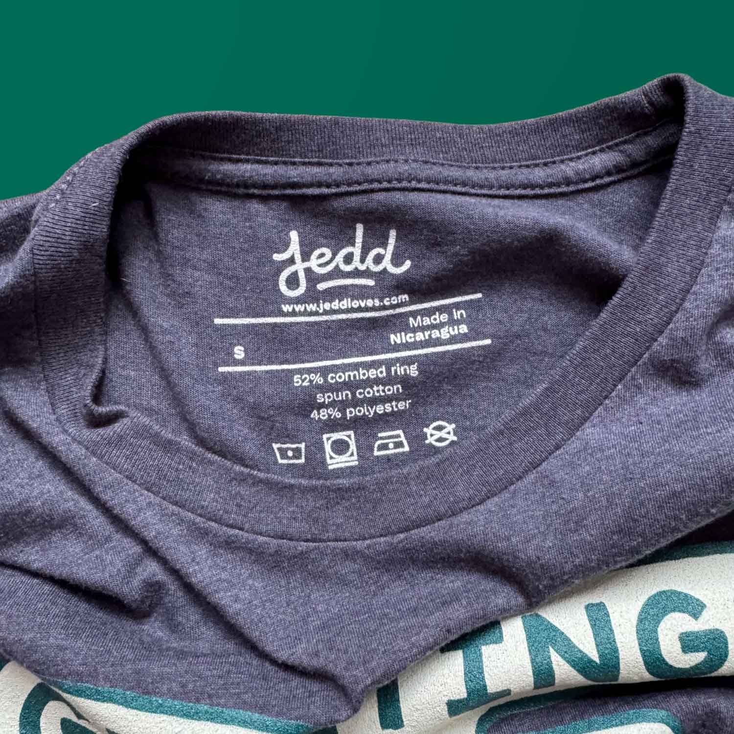 Inside neck detail of a blue t-shirt with Jedd's logo and care instructions.