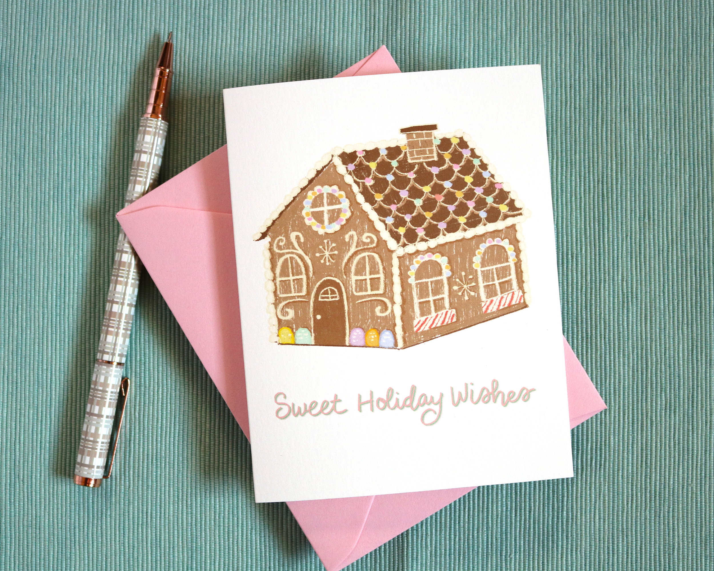 Our Pastel Gingerbread House Greeting Card features an illustrated gingerbread house decorated with pastel candies on a white background with the words “Sweet Holiday Wishes” in pink calligraphy.