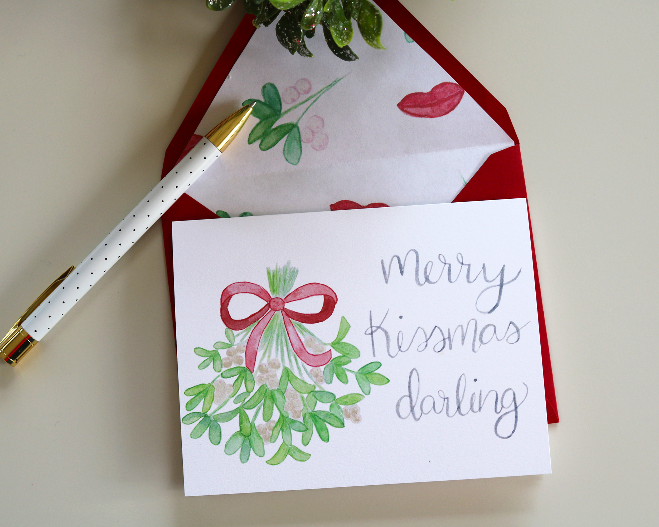 Our Watercolor Mistletoe Merry Kissmas Darling greeting card comes with a red envelope lined with watercolor mistletoe branches and lips.
