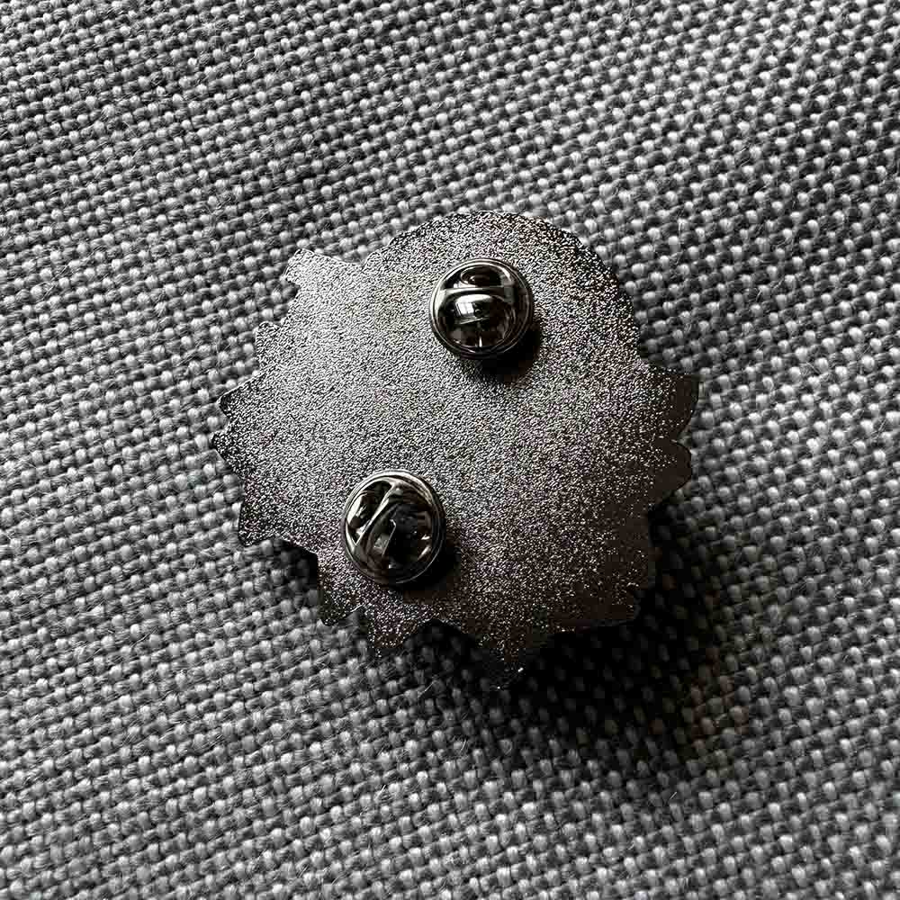 The silver backing of an enamel pin with two prongs.