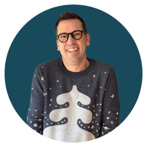 A portrait of Jedd wearing a blue sweater with a tree design