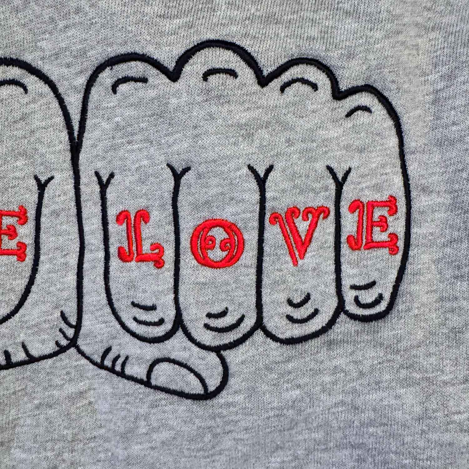 Embroidery detail of the word LOVE in a fist design on a heather gray fabric