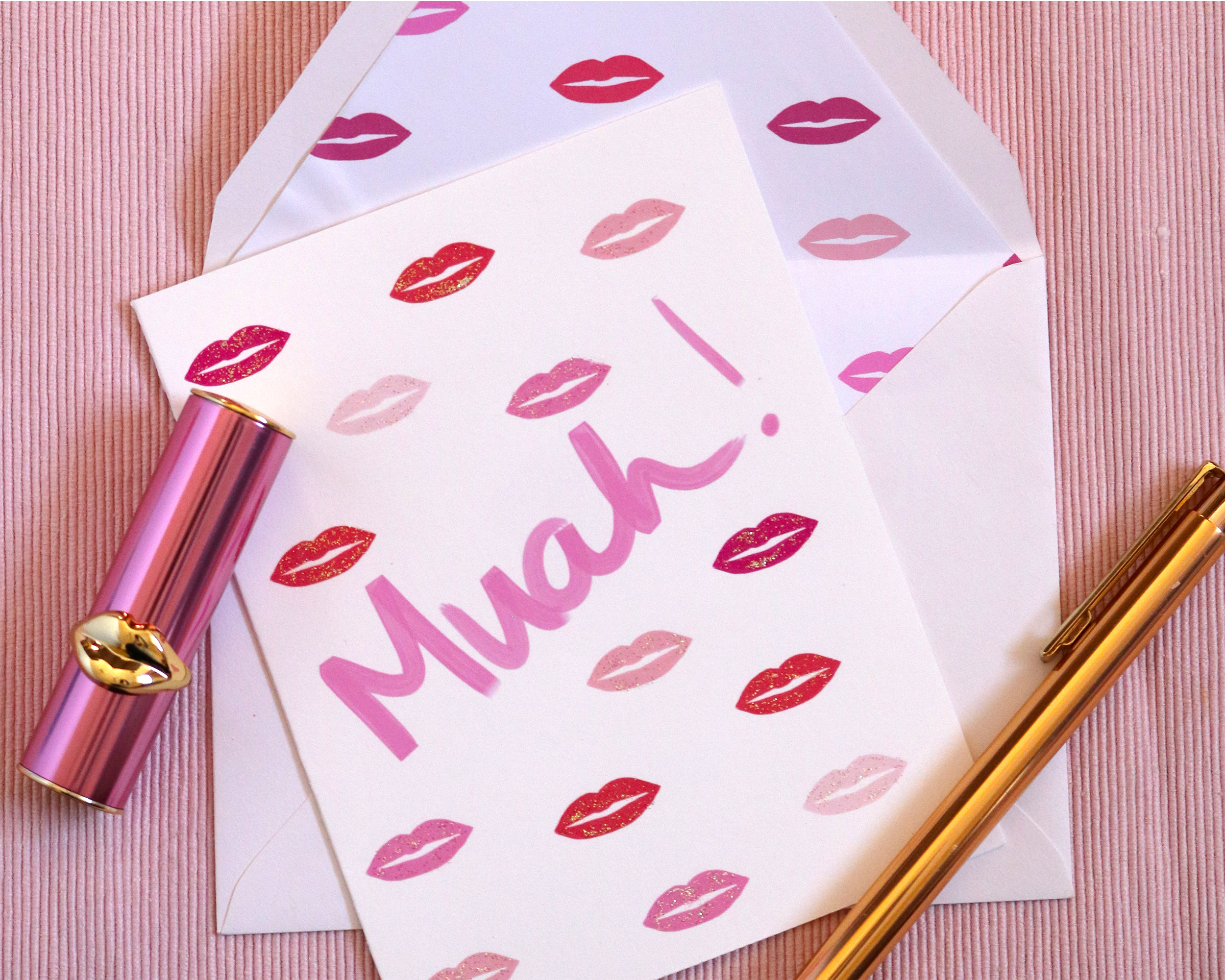 Our Muah Kiss greeting card is displayed with a white envelope. The envelope is lined with our lips pattern. The card has our illustrated lips pattern on the front and the hand lettered word muah.