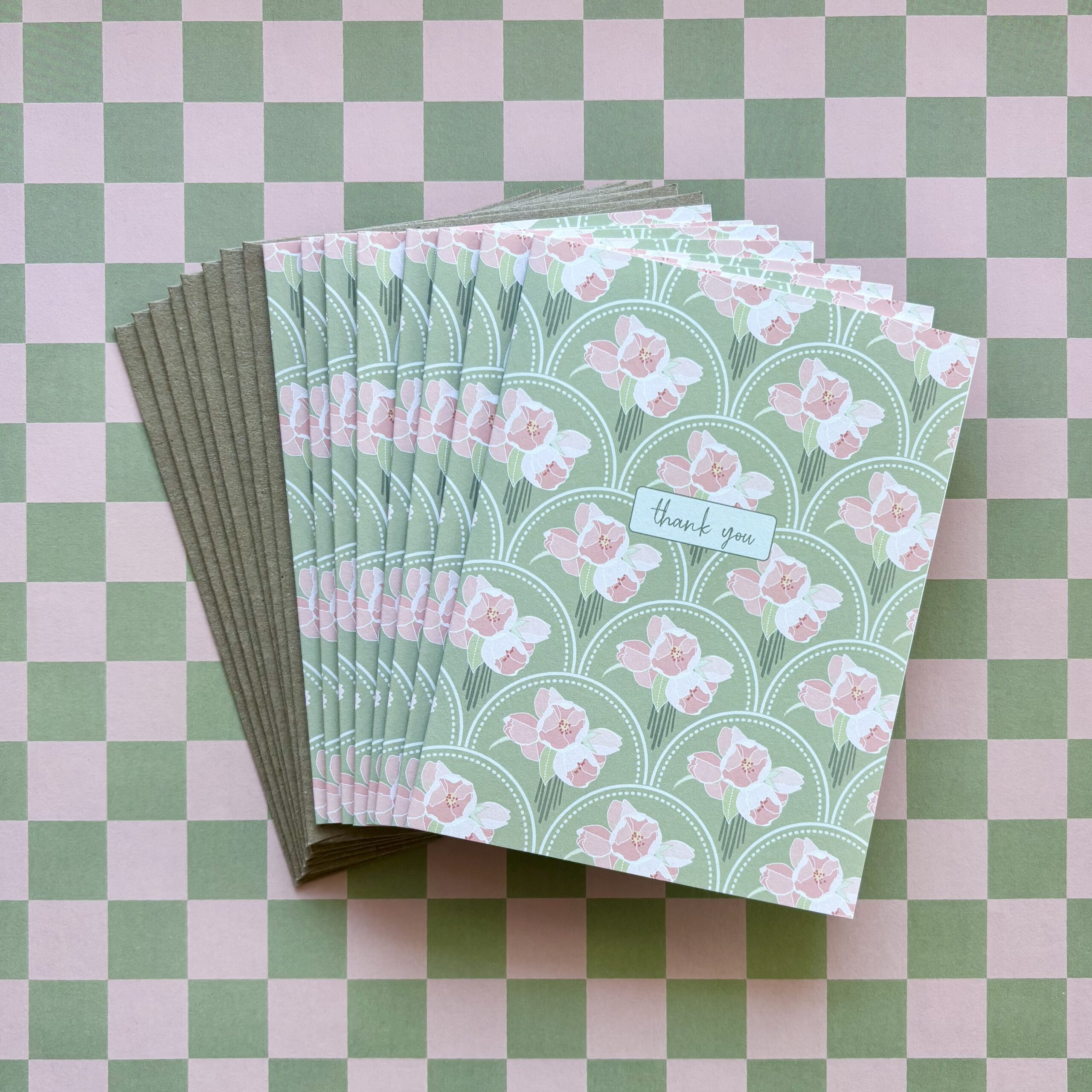Fanned stack of thank you cards with a pink and green scalloped floral pattern on a checked background