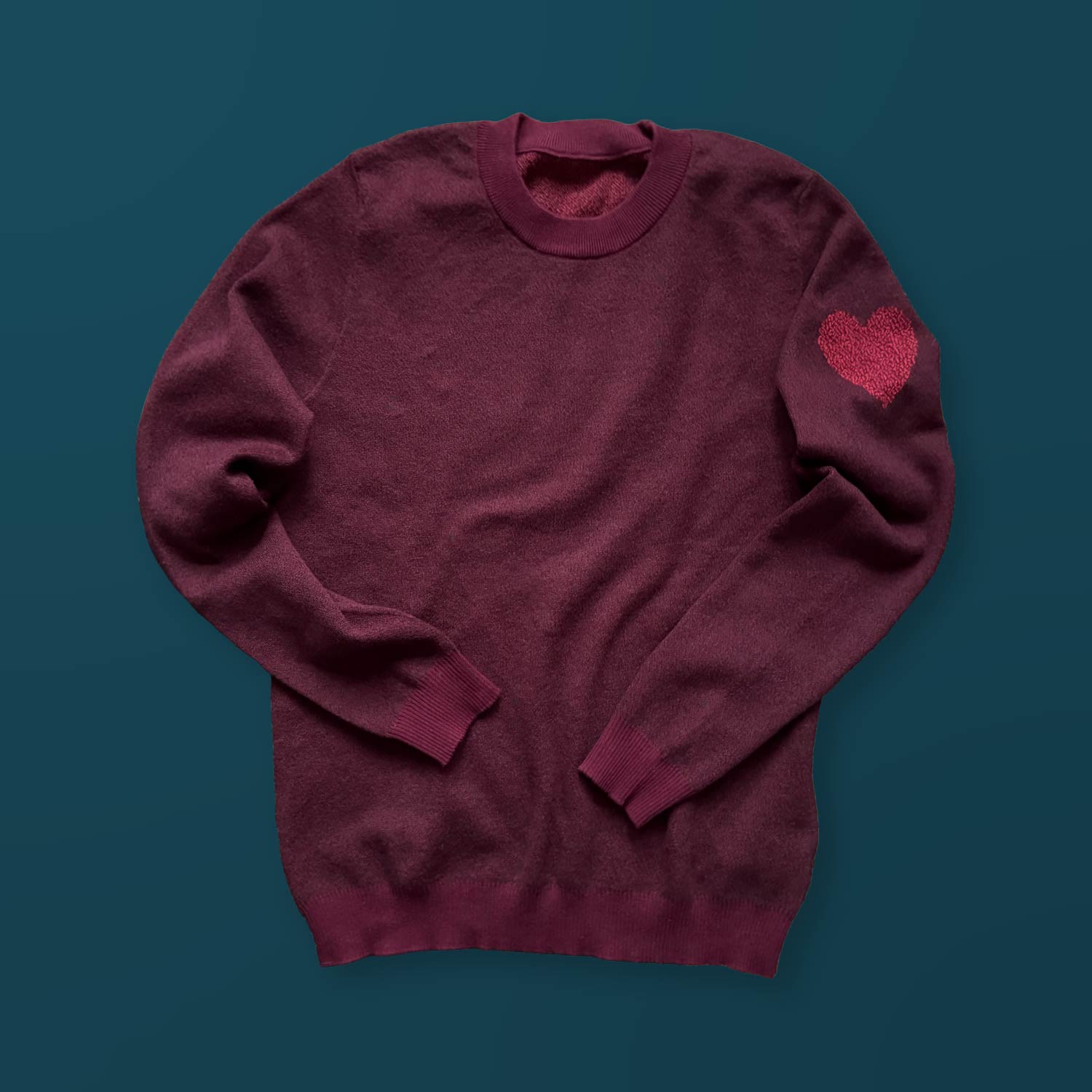 A burgundy sweater with a red heart design on the left sleeve