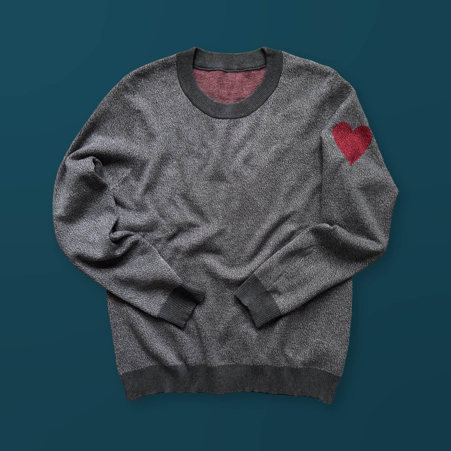 A gray sweater with a red heart design on the left sleeve