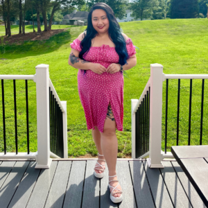 woman wearing a pink dress standing on a deck in front of grass and trees
