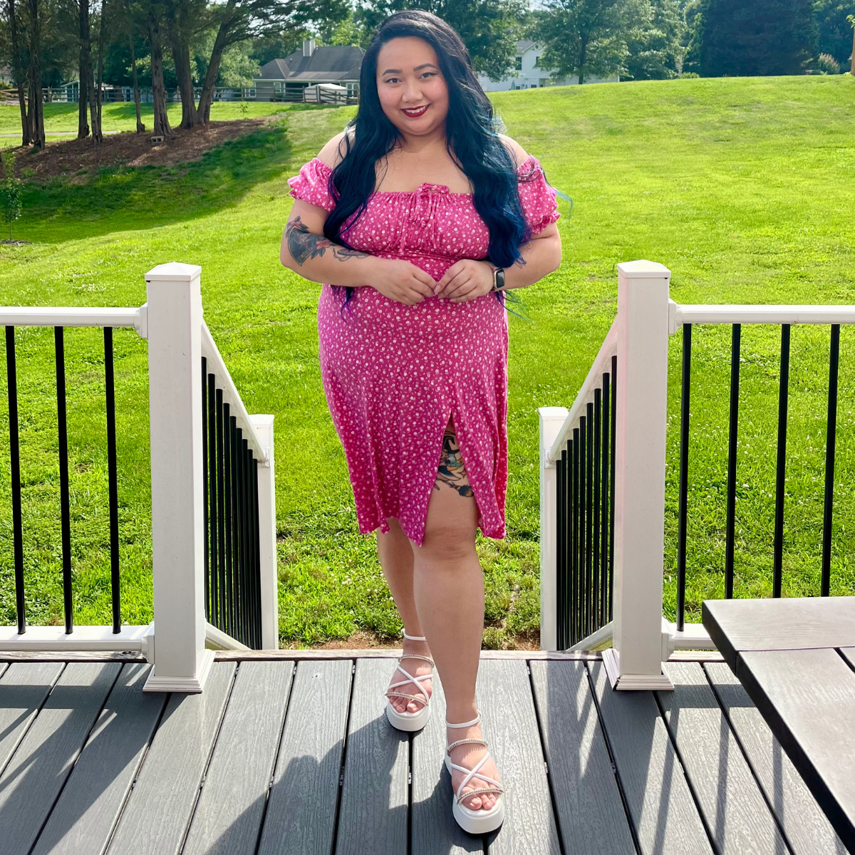 woman wearing a pink dress standing on a deck in front of grass and trees