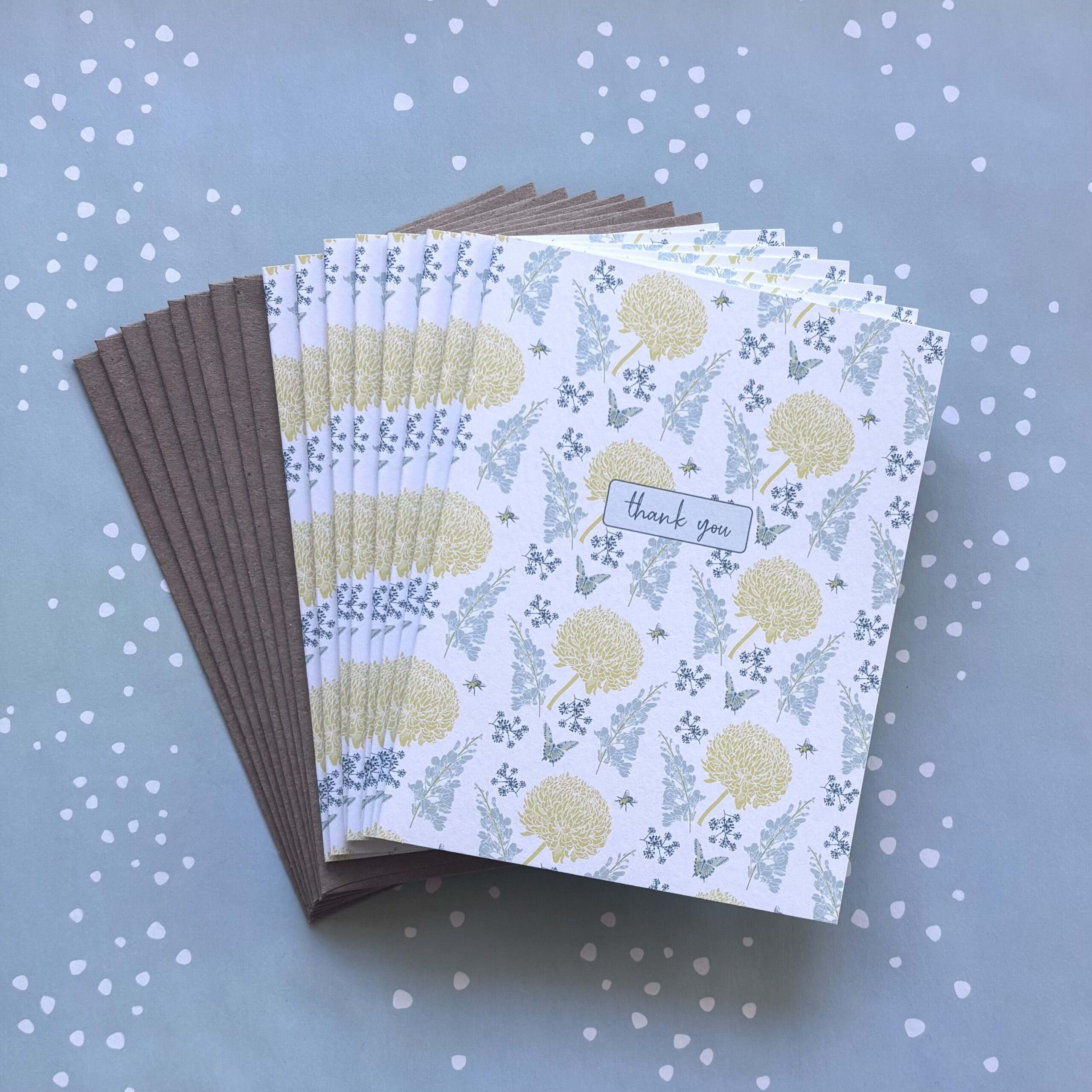 Fanned stack of eight floral print thank you cards on a blue background