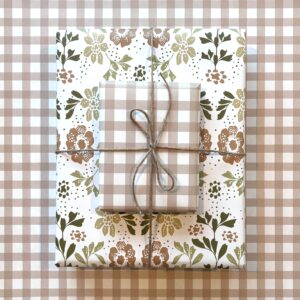 Two gift boxes with coordinating wrapping paper patterns, one is a floral in cream, tan & green, the otyher is a tan gingham plaid