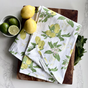 Lemon Printed tea towel styled on a wooden cutting board and kitchen counter with mint leaves, fresh lemons and limes