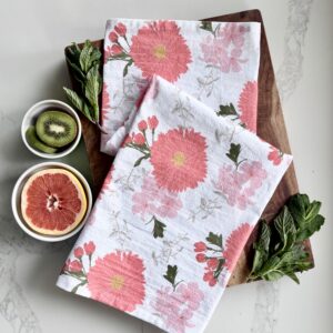 Pink floral print tea towel styled on a wooden cutting board and a kitchen counter with mint leaves and sliced grapefruit and kiwi